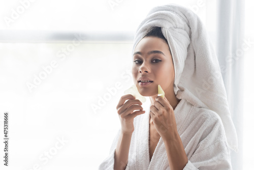 young african american woman in white towel massaging face with jade face scrapers