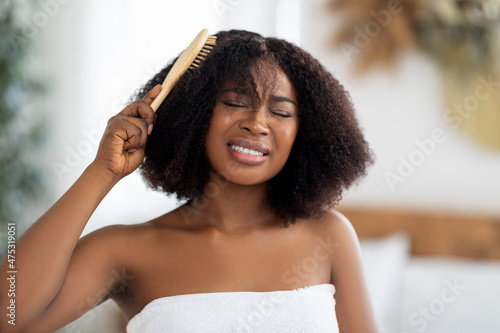 Frustrated millennial black woman trying to brush her tangled hair at home. Domestic hairdressing concept photo