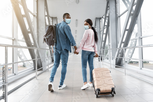 Travels During Coronavirus. Black Couple In Medical Masks Walking In Airport Terminal