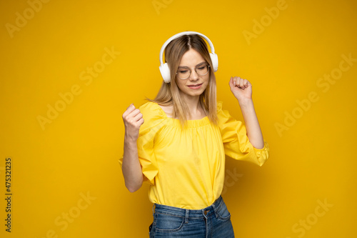 Lifestyle Concept. Portrait of beautiful woman in a glasses and yellow shirt joyful listening to music. Yellow studio background. Copy Space.