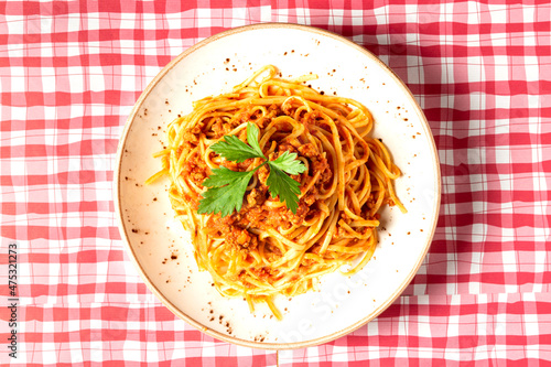 View from above of delicious spaghetti bolognese style dish decorated with a basil leaf on a red and white checkered tablecloth. Typical Italian cuisine. High quality photo photo