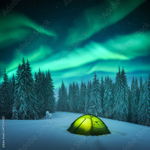 Yellow tent lighted from the inside against the backdrop of incredible starry sky with Aurora borealis. Amazing night landscape. Northern lights in winter field