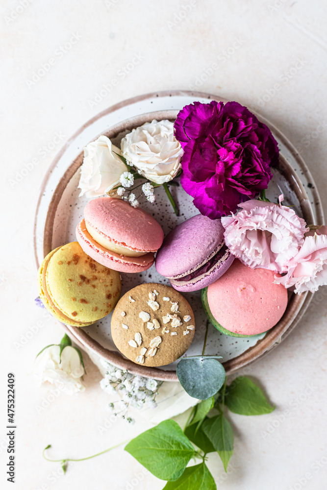 Various types of colorful macarons or macaroons decorated with flowers on light background. Traditional french almond dessert with sweet filling. Top view.