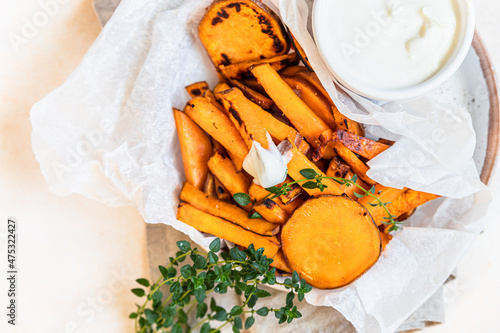 Healthy homemade baked sweet potato wedges with cream dip sauce and herbs on concrete background. Healthy snack. photo