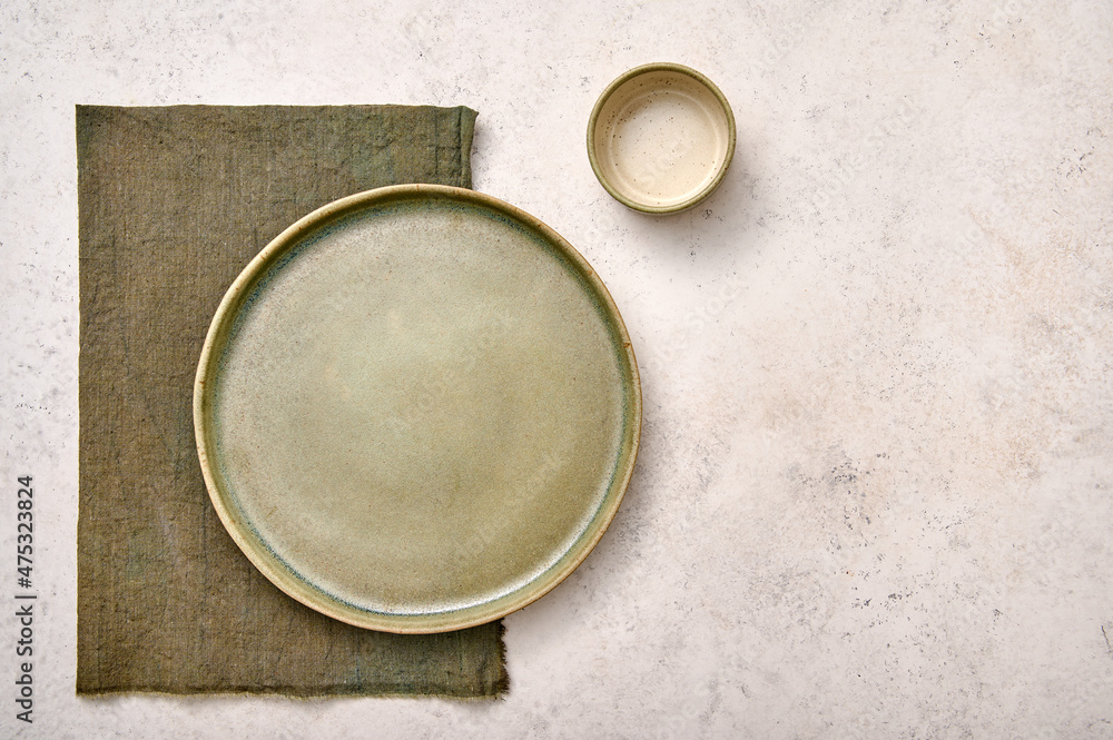 Blank green plate with napkin and saucepan on white textured background. Design concept, copy space Blank green plate with napkin and saucepan on white textured background. Design concept, copy space