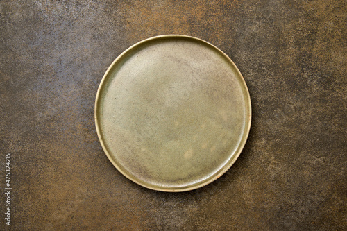 Empty green rustic ceramic plate with black rim on brown rustic background, flat lay, copy space