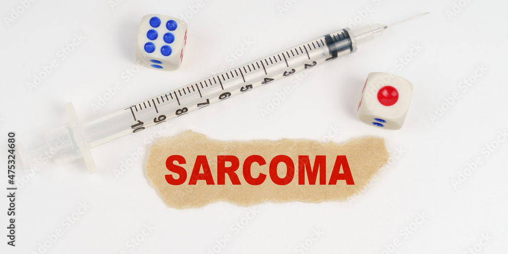 On a white surface lies a syringe, dice and a piece of paper with the inscription - SARCOMA On a white surface lies a syringe, dice and a piece of paper with the inscription - SARCOMA
