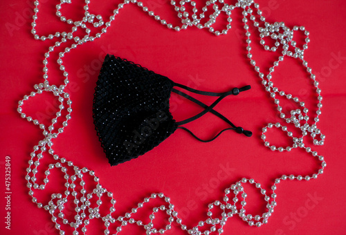 black protective face mask on red background with festive silver beads decor