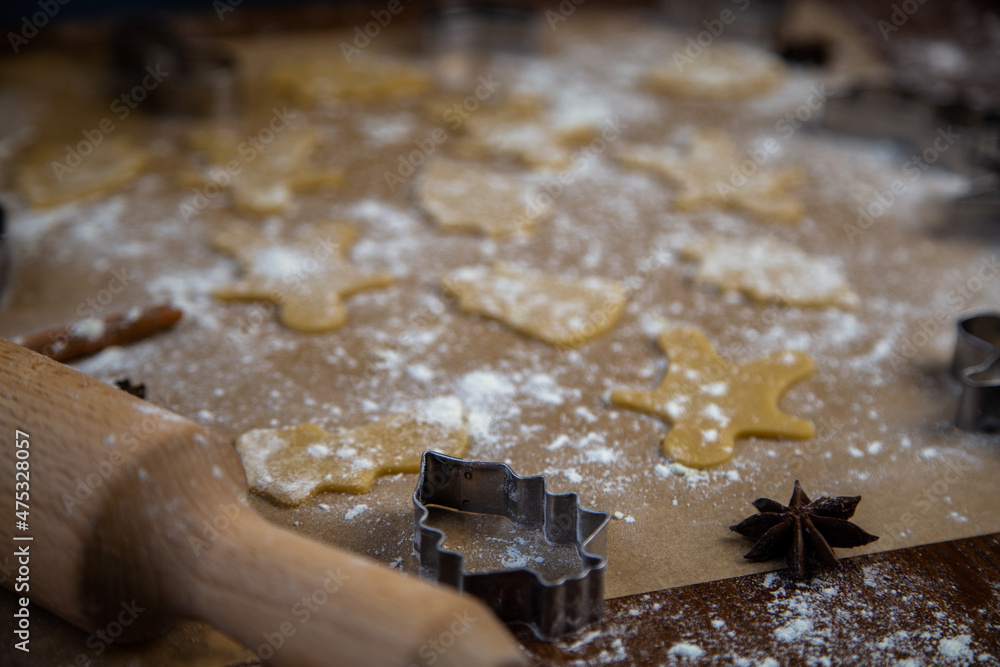 There are ready-made cookies of different shapes on the parchment, a rolling pin, cookie cutters and a sieve with flour are lying nearby, flour is scattered everywhere. High quality photo There are ready-made cookies of different shapes on the parchment, a rolling pin, cookie cutters and a sieve with flour are lying nearby, flour is scattered everywhere. High quality photo