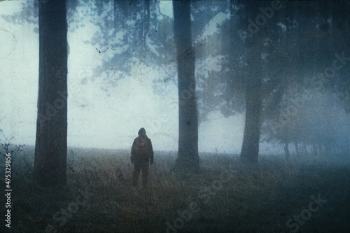 A spooky, lonely figure. Standing on the edge of an avenue of trees in the countryside. On a atmospheric winters day. With a grunge, blurred edit.