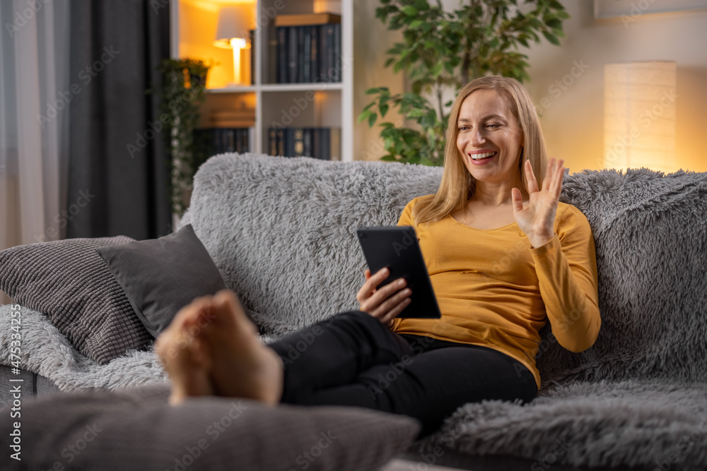 Smiling caucasian woman in casual clothes sitting on couch and having video chat on digital tablet. Happy blonde using modern gadget for online conversation from home. Smiling caucasian woman in casual clothes sitting on couch and having video chat on digital tablet. Happy blonde using modern gadget for online conversation from home.
