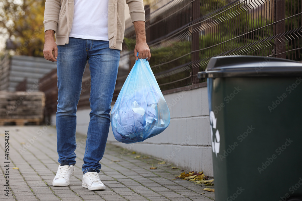 Man carrying garbage bag to recycling bin outdoors, closeup Man carrying garbage bag to recycling bin outdoors, closeup