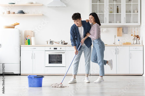 Loving asian couple mopping floor in kitchen