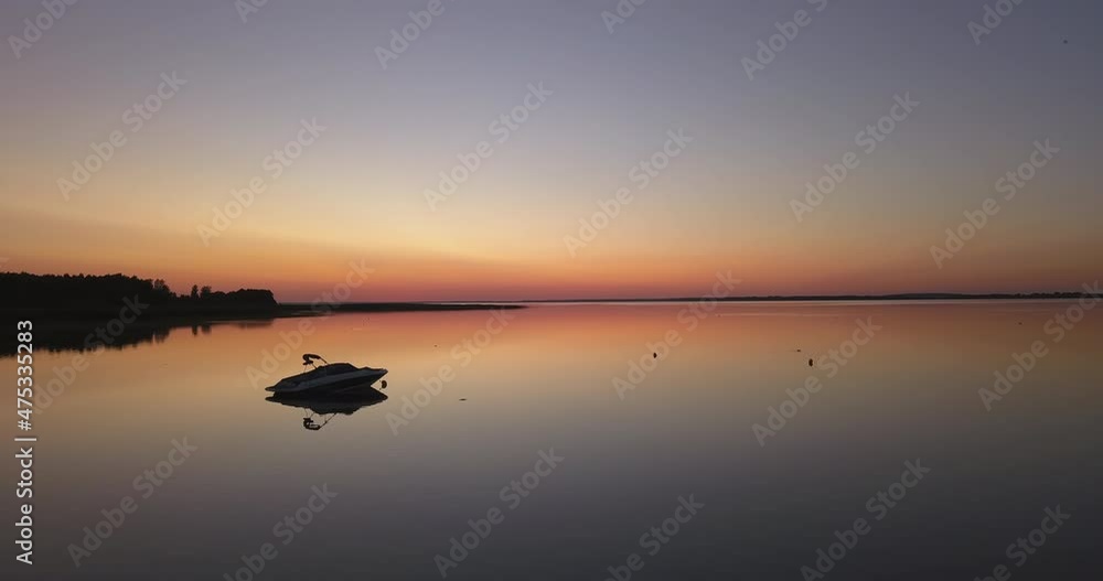 Sunset over the lake surrounded by the forest. Docked motorboat, pastel orange sky. Slow drone flight low over the water. Sunset over the lake surrounded by the forest. Docked motorboat, pastel orange sky. Slow drone flight low over the water.