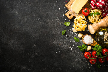 Pasta ingredients on black background. Italian food background. Pasta, parmesan, fresh tomatoes and basil with spices. Top view with copy space.