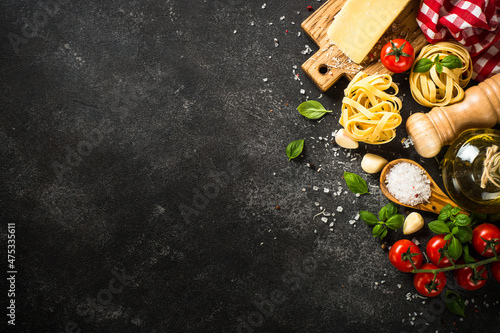 Pasta ingredients on black background. Italian food background. Pasta, parmesan, fresh tomatoes and basil with spices. Top view with copy space.