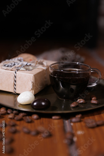 a glass cup with Americano on a gold tray. coffee beans are scattered everywhere. Cardboard box with sweets inside.