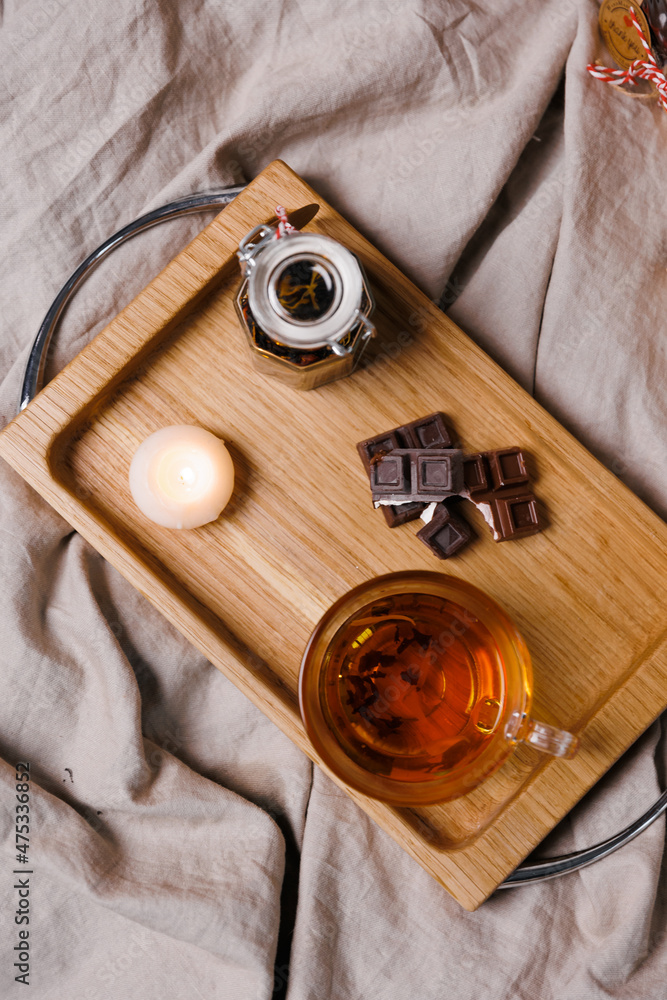 Glass mug with black tea. A wooden board, pieces of chocolate and a candle.