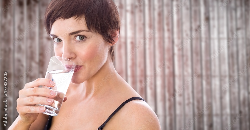 Composite image of caucasian woman drinking water from a glass against wooden background Composite image of caucasian woman drinking water from a glass against wooden background