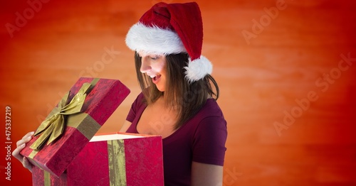 Composite image of caucasian woman wearing santa hat opening a gift against orange background