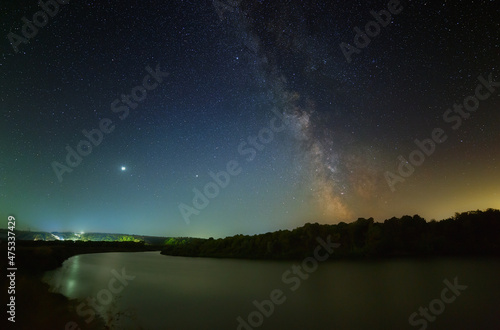 The Milky Way and the planet Jupiter in the night starry sky above the river. A wonderful place to observe nature.
