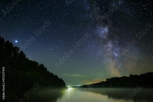 Bright stars of the Milky Way in the night sky over the river with fog. Wonderful place for landscape.