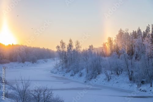 Beautiful winter landscape. Sunrise on a frozen river. The rising sun is like a candle, and a rainbow is visible on the other side of the sky. Trees are covered with hoarfrost  © Mariya Fedorova
