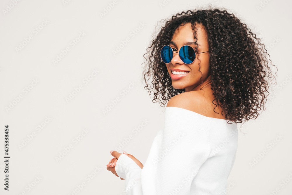 Beautiful black woman with afro curls hairstyle.Smiling model in sweater and trendy jeans clothes. Sexy carefree female posing on white background in studio. Tanned and cheerful. In sunglasses Beautiful black woman with afro curls hairstyle.Smiling model in sweater and trendy jeans clothes. Sexy carefree female posing on white background in studio. Tanned and cheerful. In sunglasses