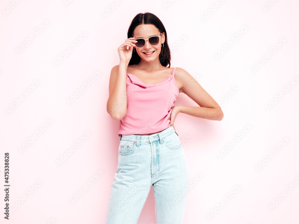 Young beautiful smiling female in trendy summer clothes. Sexy carefree woman posing near pink wall in studio. Positive model having fun indoors. Taking off sunglasses