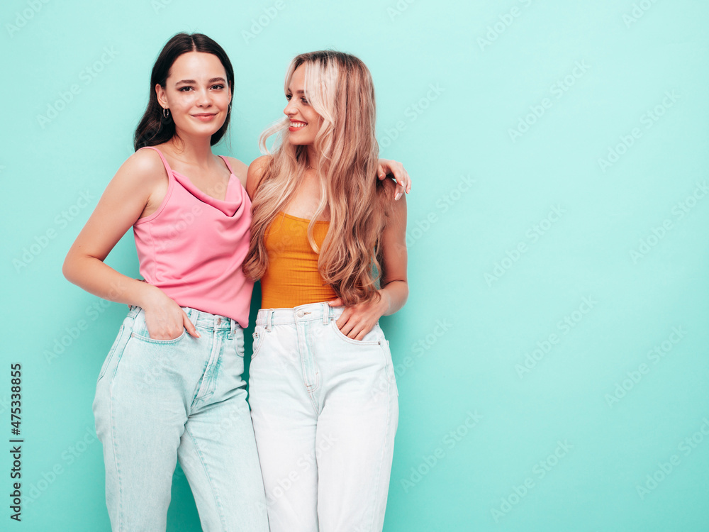 Two young beautiful smiling brunette hipster female in trendy summer clothes. Sexy carefree women posing near blue wall. Positive models having fun. Cheerful and happy Two young beautiful smiling brunette hipster female in trendy summer clothes. Sexy carefree women posing near blue wall. Positive models having fun. Cheerful and happy