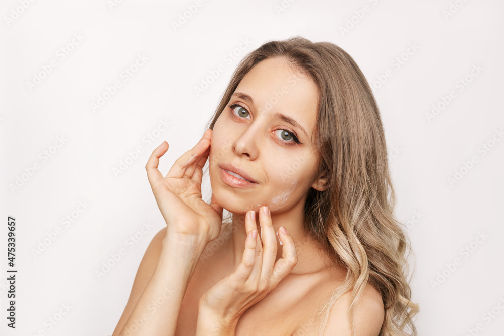 A young beautiful caucasian woman with wavy hair touching the face with her hands applying a moisturizing cream on the skin isolated on a white background. Cosmetology and beauty concept A young beautiful caucasian woman with wavy hair touching the face with her hands applying a moisturizing cream on the skin isolated on a white background. Cosmetology and beauty concept