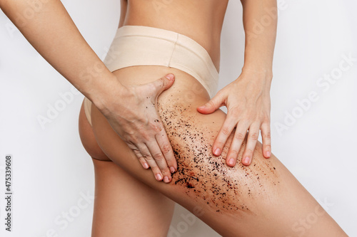 Cropped shot of young slender tanned woman massaging her thigh with a anti-cellulite coffee scrub with her hands isolated on a white background. Cosmetology, peeling, spa cosmetic products. Skin care