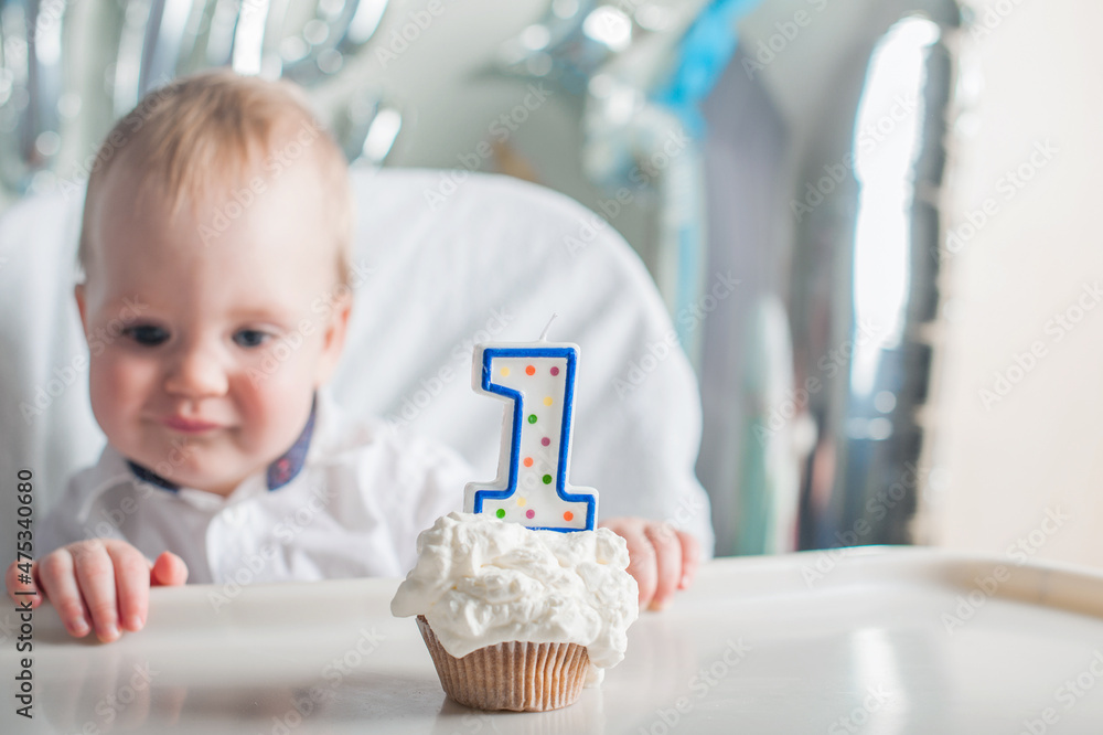 Cute toddler boy for first year of birth eating birthday cupcake with 1 candle close-up and copy space. Selective focus. Cute toddler boy for first year of birth eating birthday cupcake with 1 candle close-up and copy space. Selective focus.