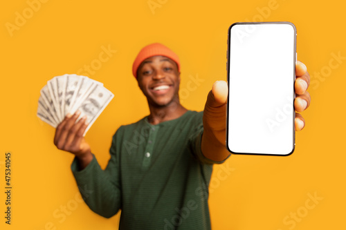 Happy Black Hipster Guy Showing Smartphone With Blank Screen And Holding Money