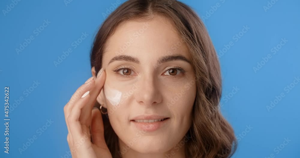 Portrait of pretty woman applying face cream on her cheek. Women's cosmetics usage. Beauty care procedures on blue screen, 4k Prores HQ Portrait of pretty woman applying face cream on her cheek. Women's cosmetics usage. Beauty care procedures on blue screen, 4k Prores HQ