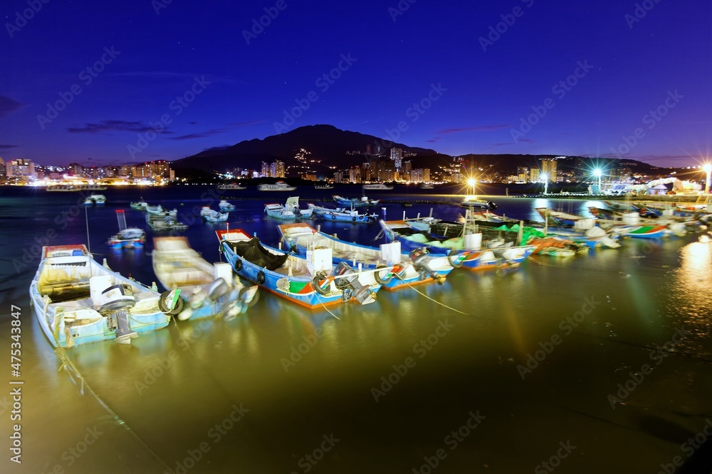 Sunrise scenery of Tamsui River in suburban Taipei, Taiwan, with ferries and fishing boats parking on the peaceful water in morning twilight and city lights glowing under beautiful dawning sky