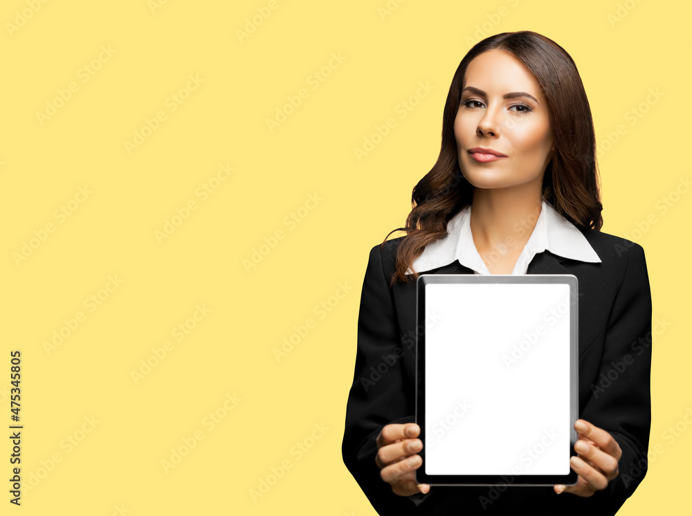 Portrait of happy smiling brunette businesswoman showing tablet pc, touchpad, with copy space for text, isolated over yellow colour background. Confident beautiful young business woman at studio Portrait of happy smiling brunette businesswoman showing tablet pc, touchpad, with copy space for text, isolated over yellow colour background. Confident beautiful young business woman at studio