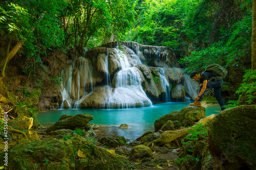 Side view shot of young man with backpack standing near a waterfall in forest. Male hiker in the nature during rain