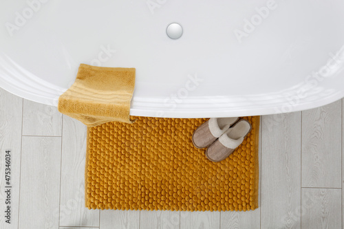 Soft orange bath mat and slippers on floor in bathroom, top view photo