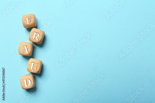 Word Fraud of wooden cubes with letters on light blue background, flat lay. Space for text