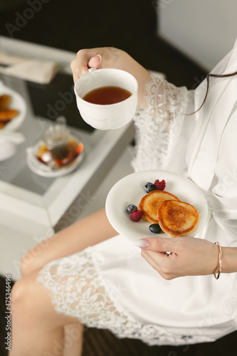 Morning of the bride. A woman is holding a mug of tea and pancakes with berries.