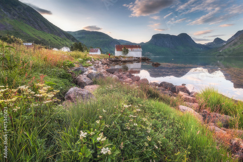 Scenic view of an authentic Norwegian house. A white dilapidated house stands on the shore of the fjord. The bay Epic clouds. A stone wall is under the house. Northern nature. Norway. Europe.