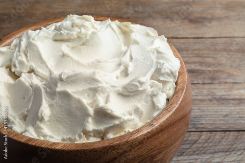 Bowl of tasty cream cheese on wooden table, closeup