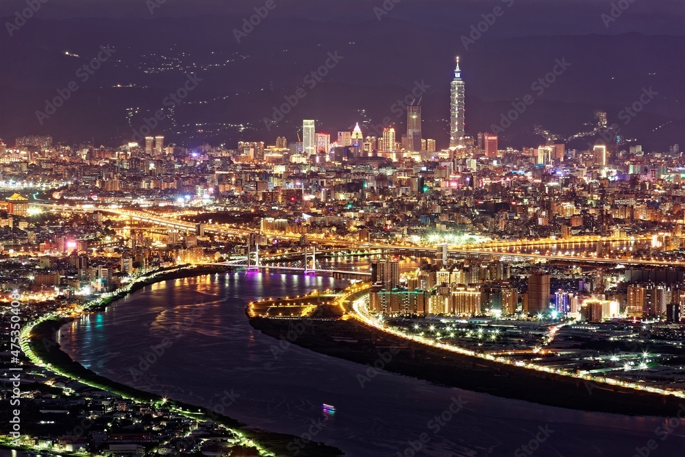 Fototapeta premium Aerial panorama over Taipei, capital City of Taiwan, on a blue gloomy evening with view of Tamsui & Keelung River, Taipei 101 Tower among high rise buildings & bright city lights in Downtown at dusk
