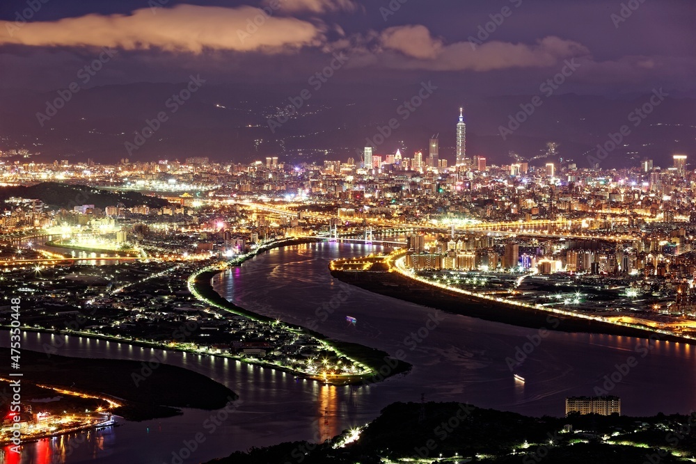 Aerial panorama over Taipei, capital City of Taiwan, on a blue gloomy evening with view of Tamsui & Keelung River, Taipei 101 Tower among high rise buildings & bright city lights in Downtown at dusk