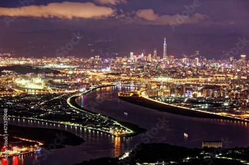 Aerial panorama over Taipei, capital City of Taiwan, on a blue gloomy evening with view of Tamsui & Keelung River, Taipei 101 Tower among high rise buildings & bright city lights in Downtown at dusk