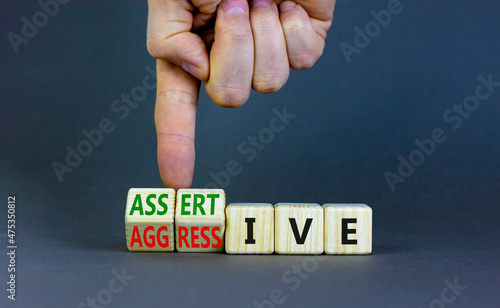 Aggressive or assertive symbol. Businessman turns wooden cubes, changes the word Aggressive to Assertive. Beautiful grey background, copy space. Business, psychological aggressive assertive concept. photo