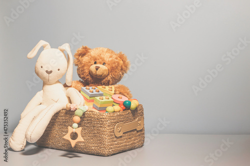 Toy box full of baby kid toys. Container with teddy bear, wooden rattles, stacking pyramid and wood blocks on light gray background. Cute toys collection for small children. Front view