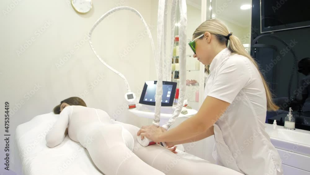 LPG massage in the beauty center.A beautiful female client in a special white suit receiving an anti-cellulite massage in a beauty salon.Hardware massage,Weight loss,Body care.Beauty salon,Lipomassage LPG massage in the beauty center.A beautiful female client in a special white suit receiving an anti-cellulite massage in a beauty salon.Hardware massage,Weight loss,Body care.Beauty salon,Lipomassage