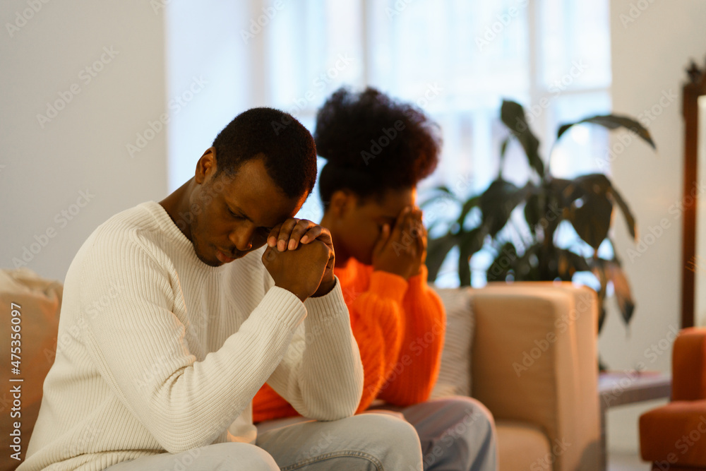 Upset pensive african american couple after fight sitting on couch separately thinking of family or relationship crisis, conflict. Offended man and woman avoid looking at each other, selective focus Upset pensive african american couple after fight sitting on couch separately thinking of family or relationship crisis, conflict. Offended man and woman avoid looking at each other, selective focus